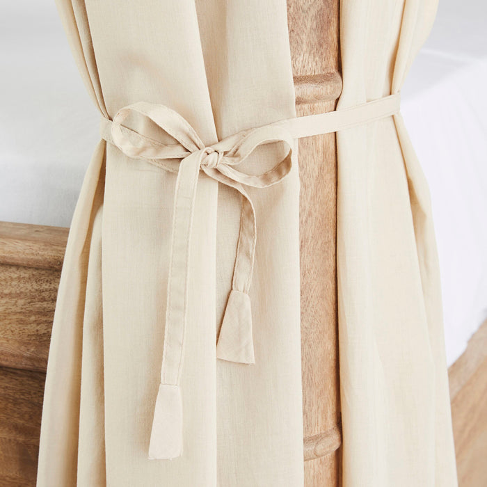 A Hampton Cotton Voile Curtain, in beige and part of a set of 6, elegantly ties around a wooden bedpost, evoking the look of neutral canopy bed curtains.
