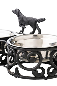The Double Dog Bowl 35x17cm features a decorative and durable iron holder with two stainless steel bowls, showcasing an antique black and silver finish and adorned with a charming metal dog silhouette on top.