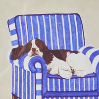 The Springer On Blue Framed Print 40x40cm depicts a charming Springer Spaniel peacefully sleeping on a blue and white striped armchair, capturing the serene essence of Carol Dillon art.