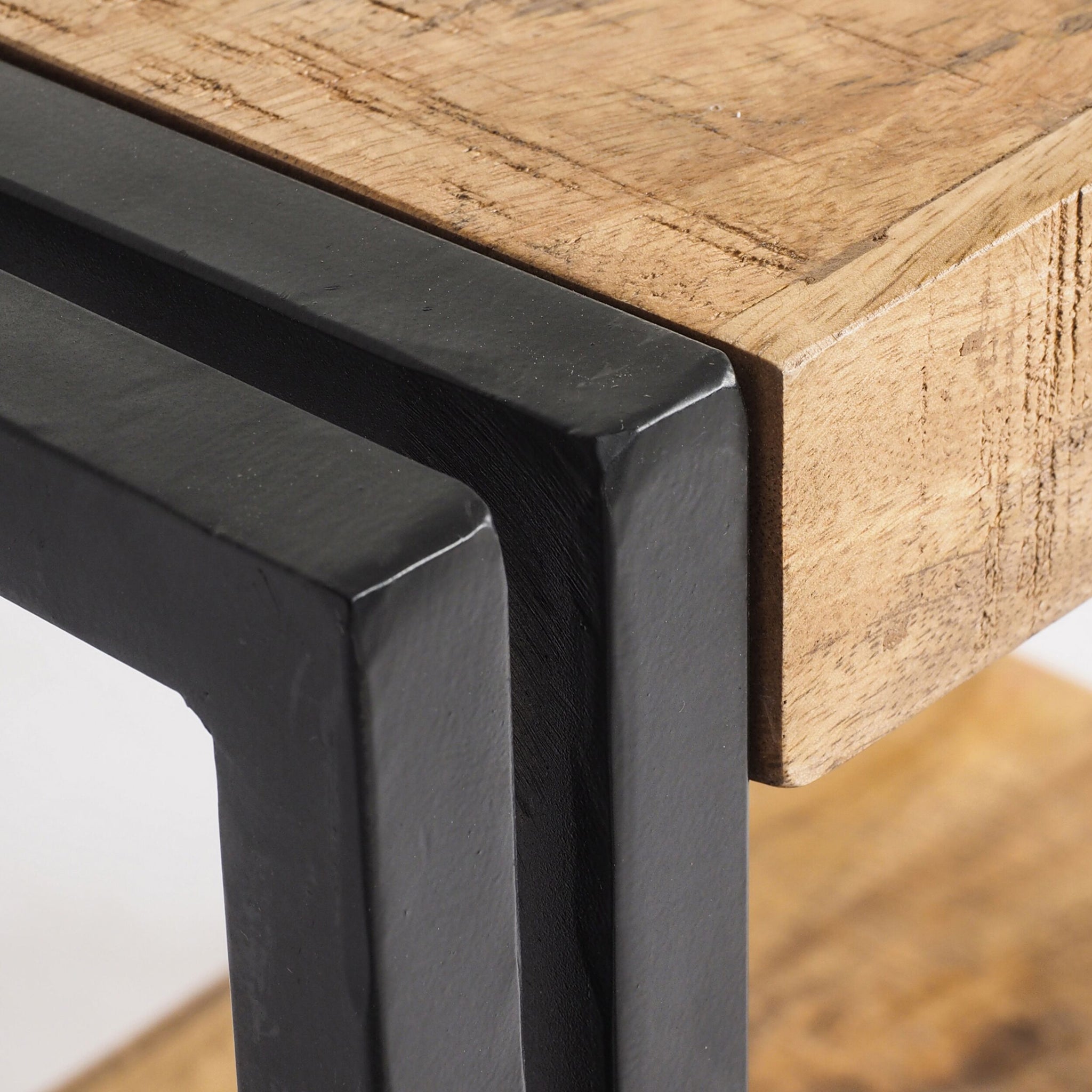 This close-up captures the Fulham Side/Bedside Table, showcasing where the textured mango wood top seamlessly meets the sleek black steel frame legs, adding a contemporary edge to its design.