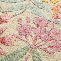 A close-up of the Botanic Native Rug 240x150cm highlights its hand-tufted 100% wool texture, featuring pink flowers and green leaves on a beige background.