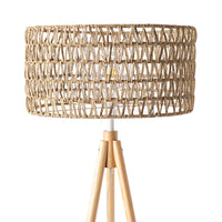 The Lexi Seagrass Natural Tripod Floor Lamp (165x45cm) features a woven rattan drum shade and wooden tripod legs, inspired by coastal living, shown against a white background.