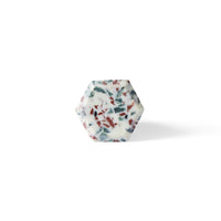 The Speckle Geo Knob 3.8cm features a hexagonal shape, white base, and embedded red and green specks—ideal as a decorative cabinet knob, shown here against a plain white background.