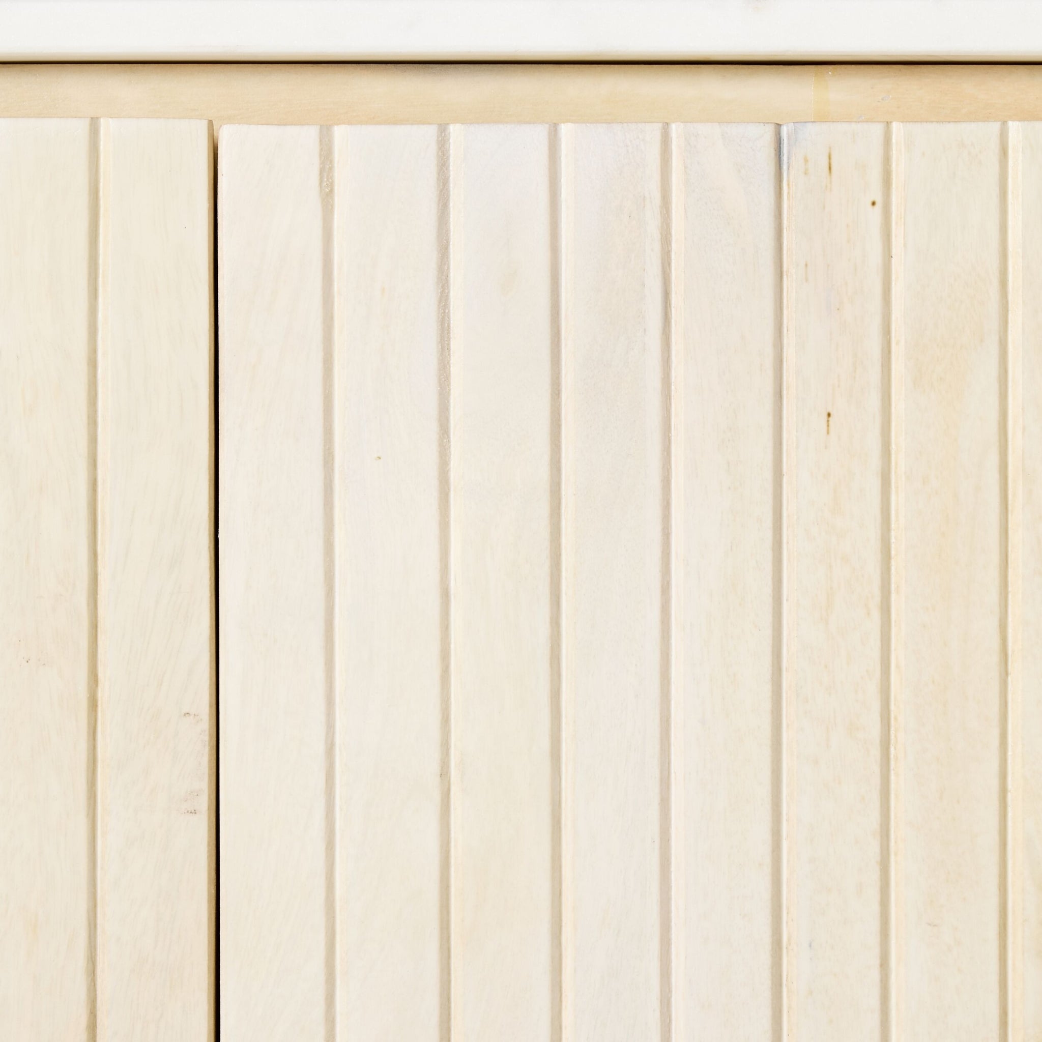 A close-up of a wooden panel with vertical grooves reveals a light, natural texture, reminiscent of the whitewashed mango wood finish of the Deva 2 Door Buffet 114 x 80 x 43cm, highlighting its refined elegance and subtle charm.