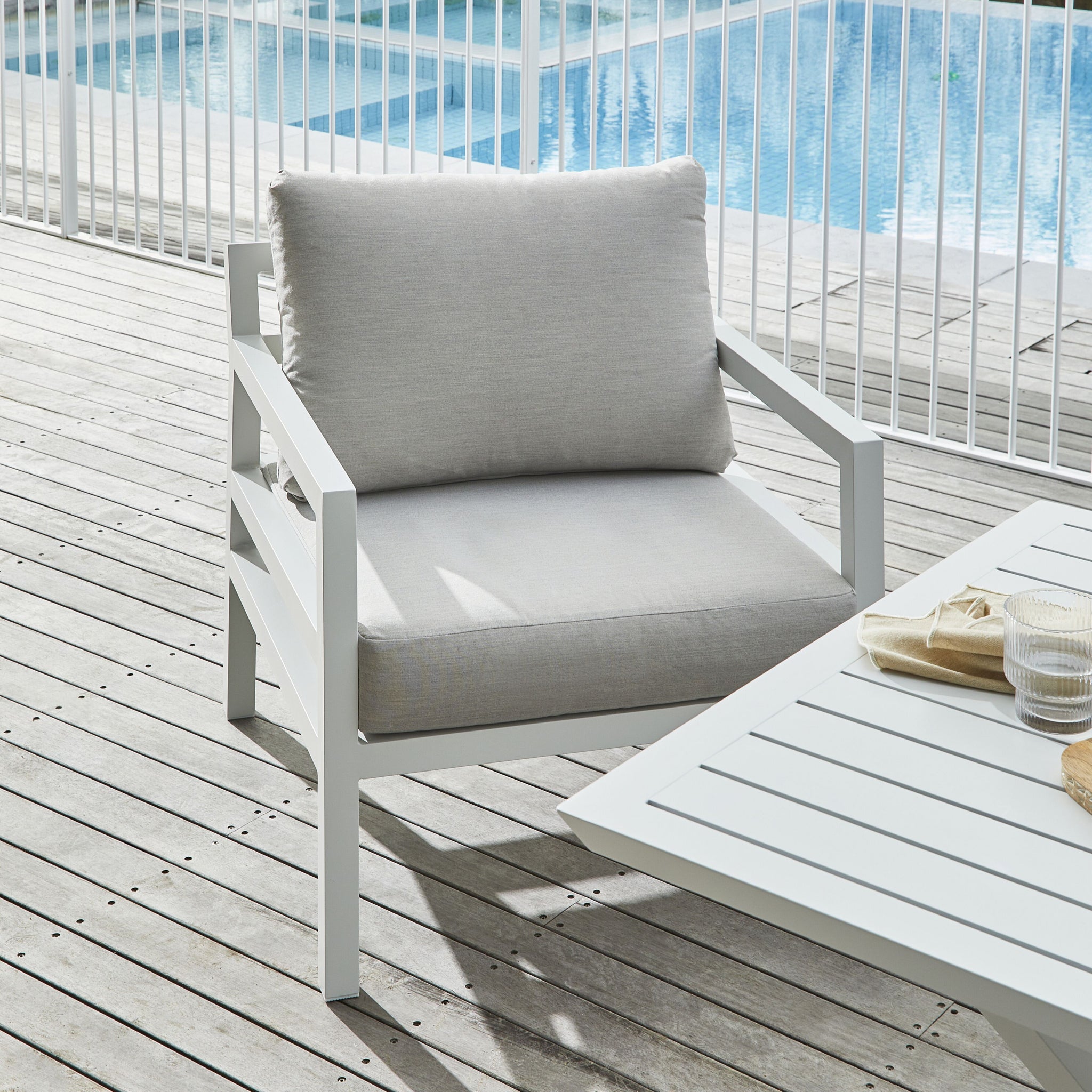 Close-up of a light gray cushioned outdoor sofa with white frame and decorative floral and striped throw pillows.