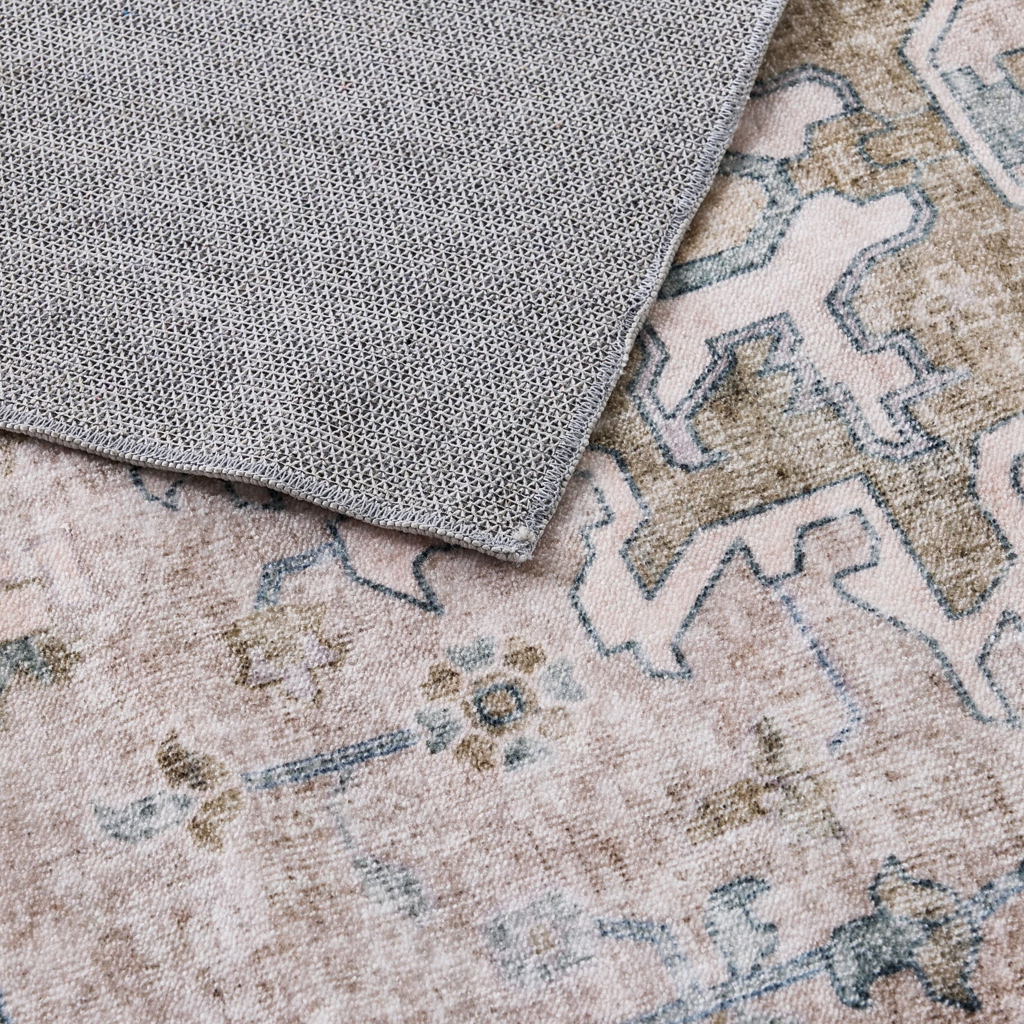 Close-up of the Manisa Washable Rug 240x300cm, featuring a grey textured cloth on a Persian-inspired rug with faded pastel colors and geometric patterns, crafted from durable, machine-washable polyester for easy care.