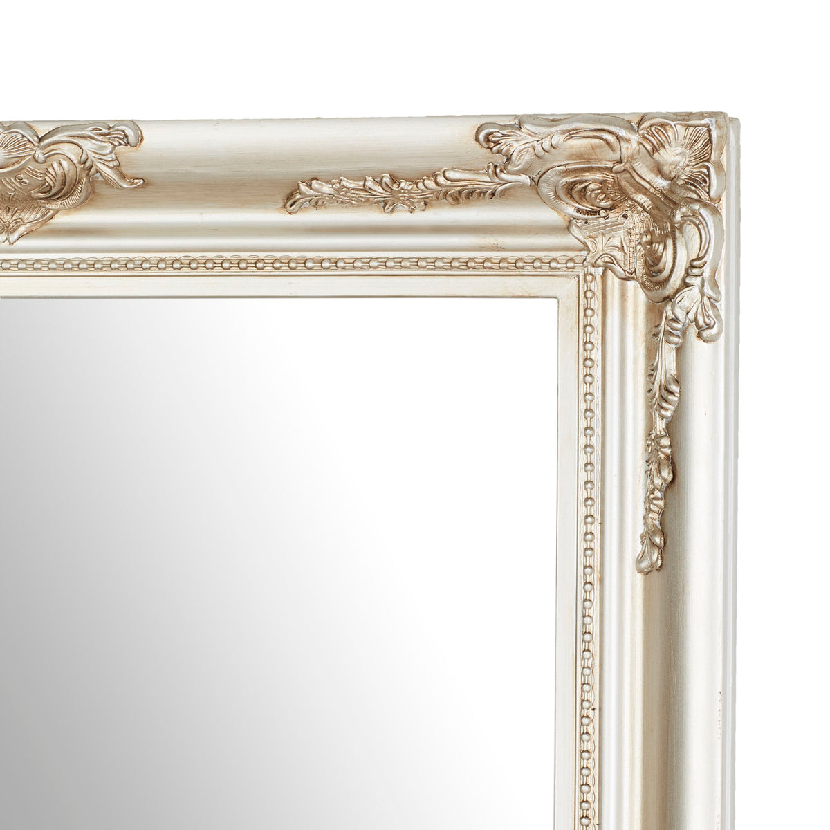 A close-up of a corner of the Jane Mirror Champagne Silver 167x77cm reveals its ornate, antique-style gold frame with intricate detailing on a plain reflective surface, highlighting its champagne silver mirror finish.