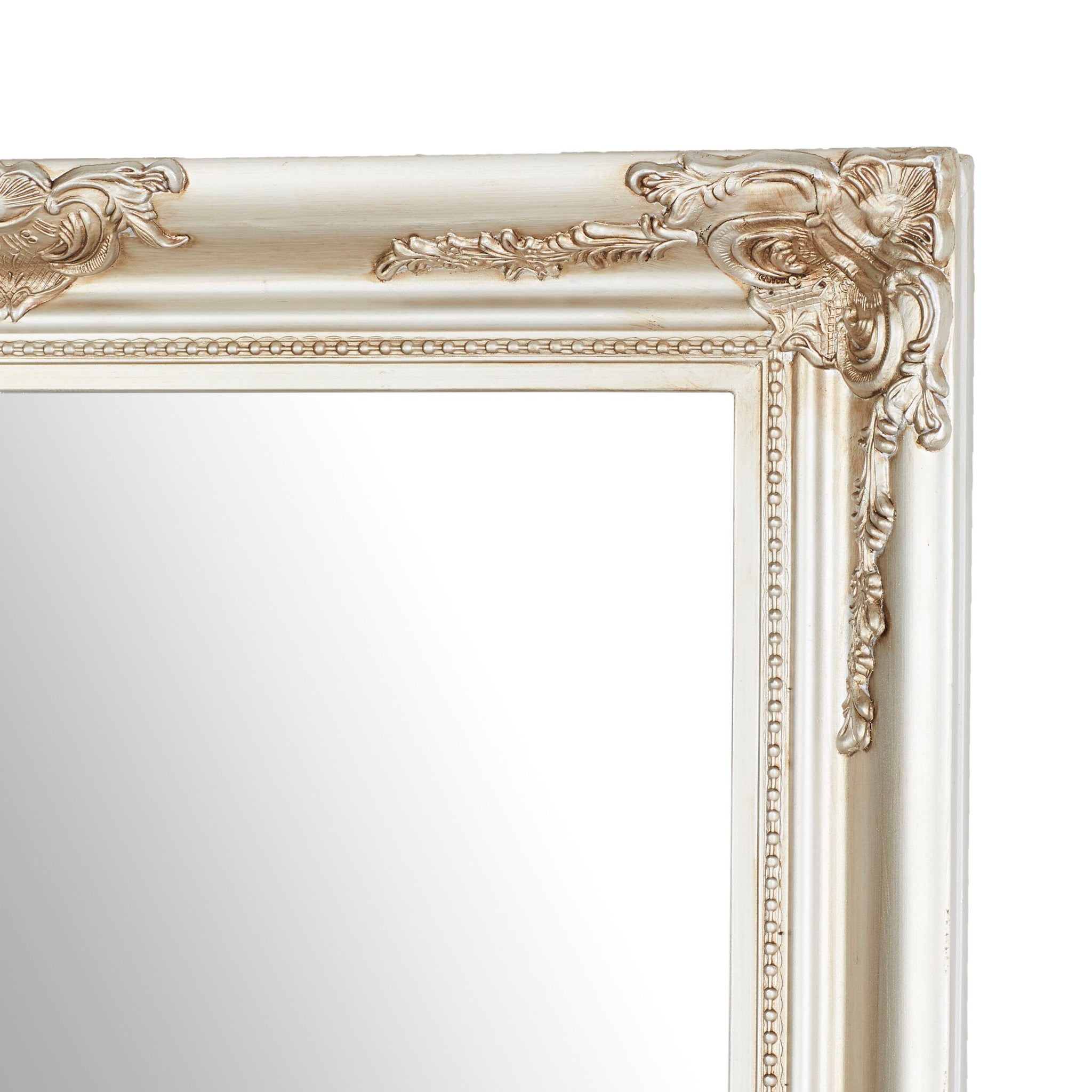 A close-up of a corner of the Jane Mirror Champagne Silver 167x77cm reveals its ornate, antique-style gold frame with intricate detailing on a plain reflective surface, highlighting its champagne silver mirror finish.